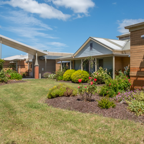 Single‑storey brick building with landscaped garden, lawn, and covered entrance under a blue sky.